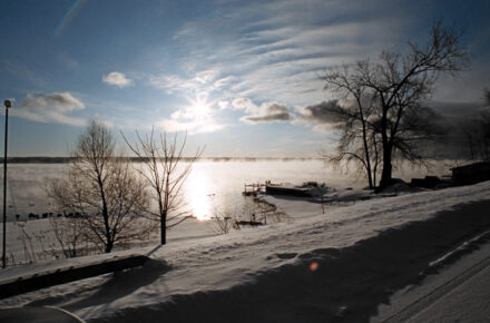 Winter scene of Cayuga Lake with snow and ice as filtered sun shines across the lake